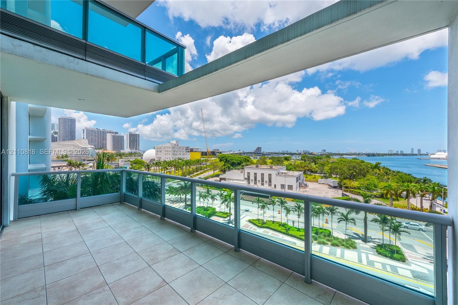Private balcony with ceramic tile flooring and glass panel railings overlooking a waterfront cityscape