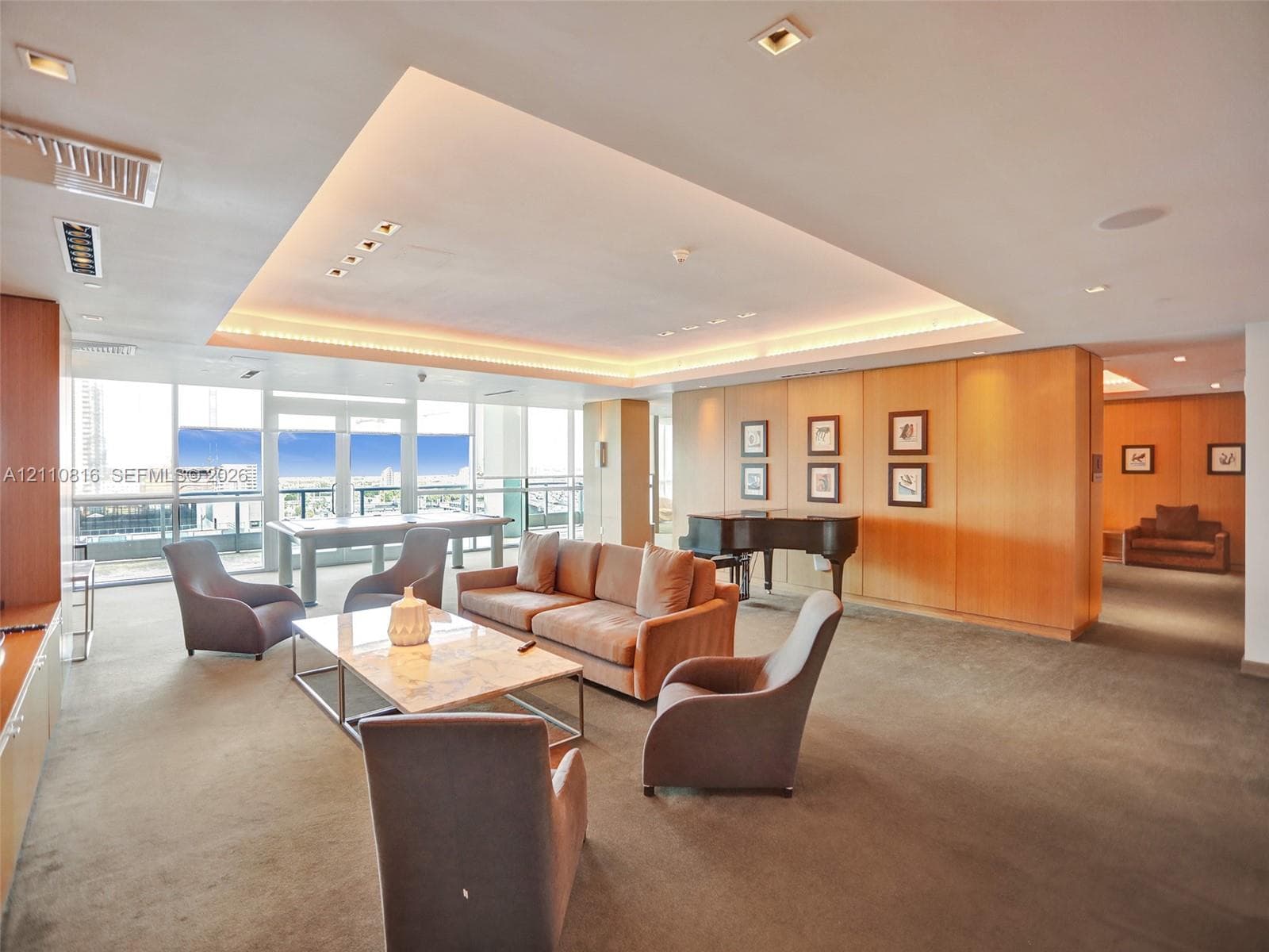 Expansive living area featuring a tray ceiling with integrated recessed lighting, floor-to-ceiling windows, and wood-paneled walls