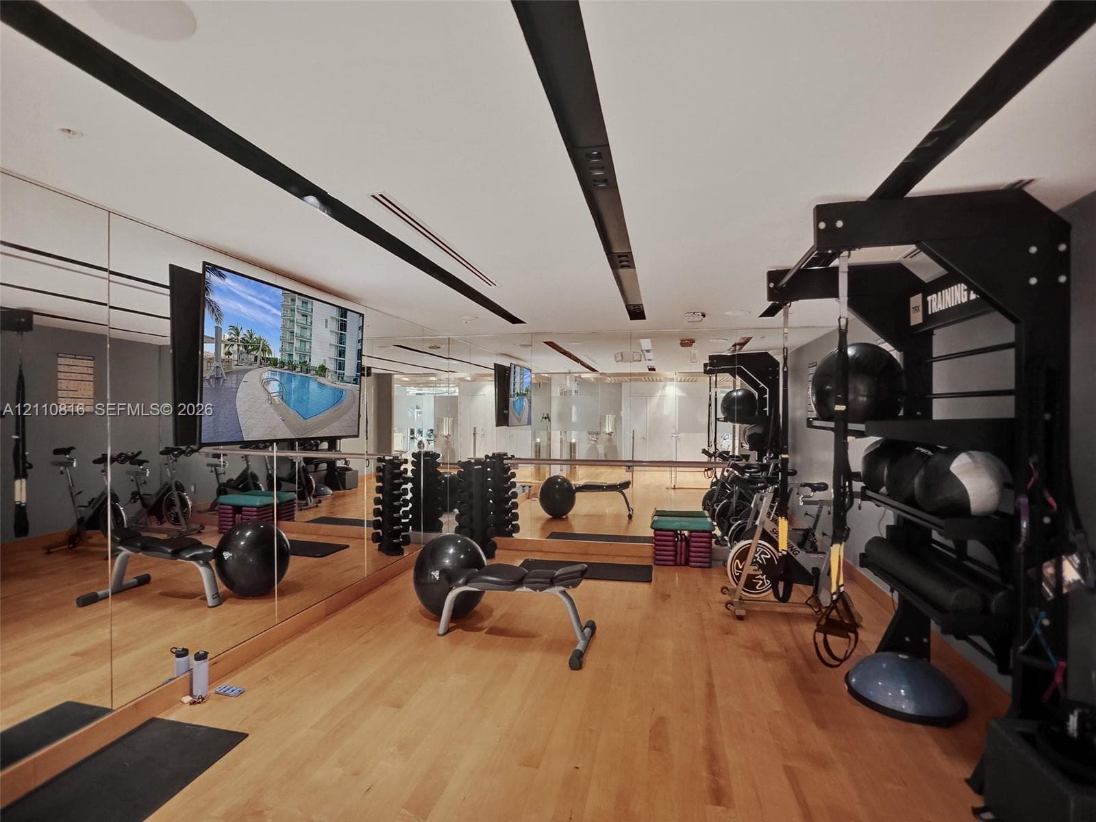 Fitness space featuring wood-finish flooring, extensive floor-to-ceiling mirrored walls, and recessed ceiling lighting