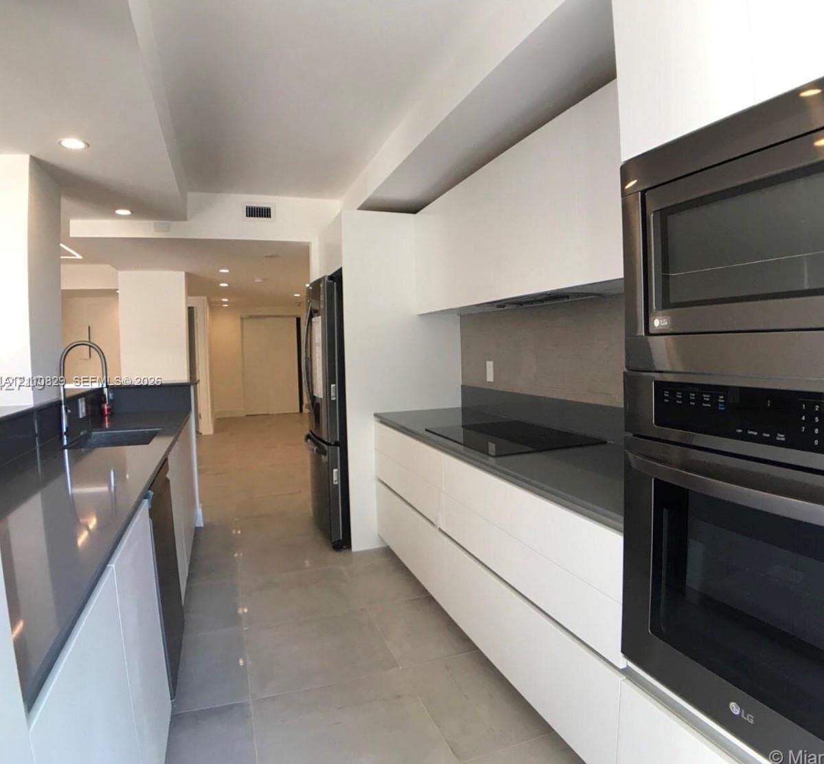 Sleek kitchen featuring flat-panel white cabinetry, quartz countertops, a smooth-surface cooktop, stainless steel wall-mounted oven and microwave, and large-format floor tile