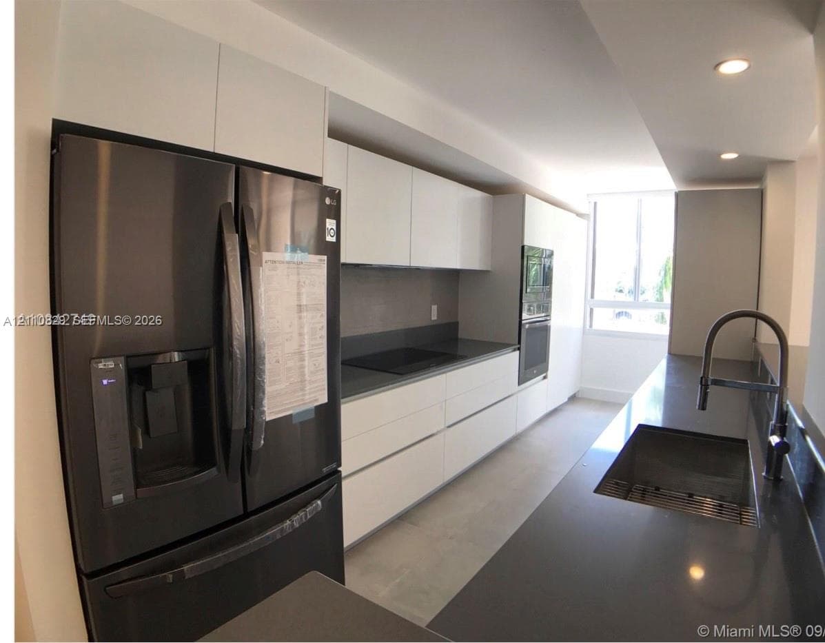 Modern kitchen featuring high-gloss white flat-panel cabinetry, dark solid-surface countertops, built-in stainless steel oven, integrated cooktop, and a matte black gooseneck faucet