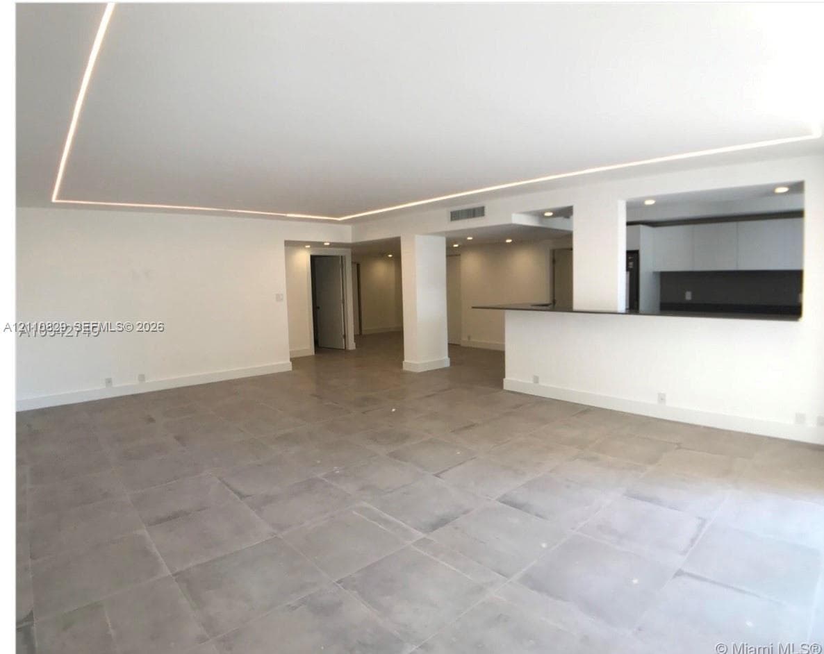 Open-concept interior featuring large-format tile flooring, recessed ceiling lighting with perimeter accent strips, and a pass-through kitchen counter