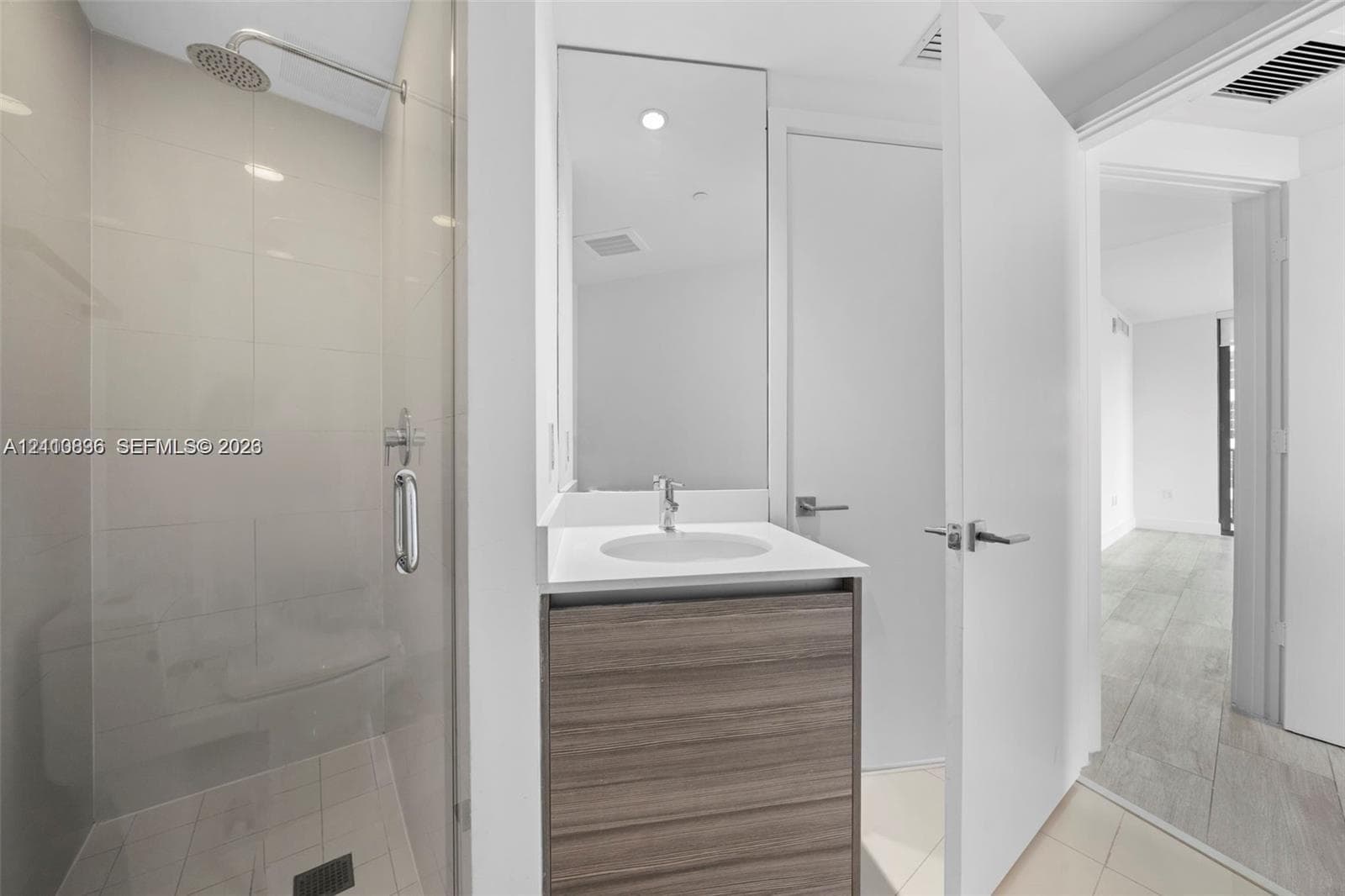 Glass-enclosed shower with rainfall showerhead, wood-finish vanity with countertop basin, and large-format tile flooring