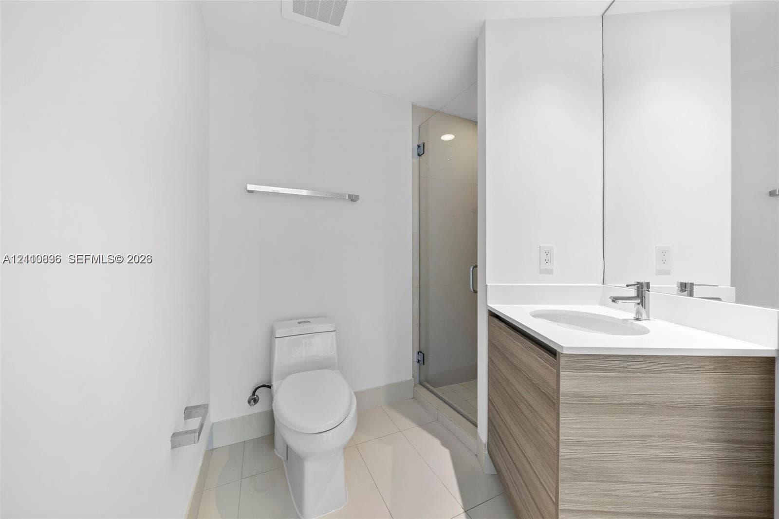 Modern bathroom featuring a floating wood-finish vanity with an integrated sink and chrome faucet, white quartz countertop, large mirror with integrated lighting, and a walk-in shower with glass enclosure