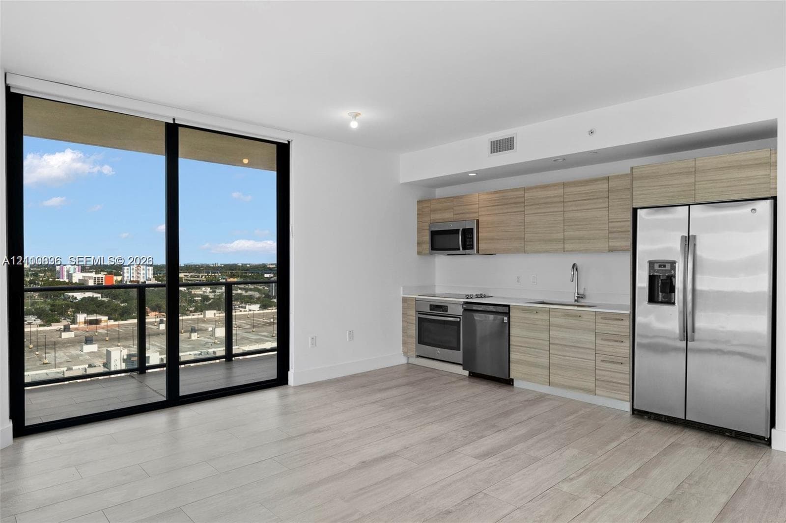 Kitchen featuring wood-finish cabinetry, stainless steel appliances, and quartz countertops, complemented by wood-finish flooring and floor-to-ceiling glass paneling