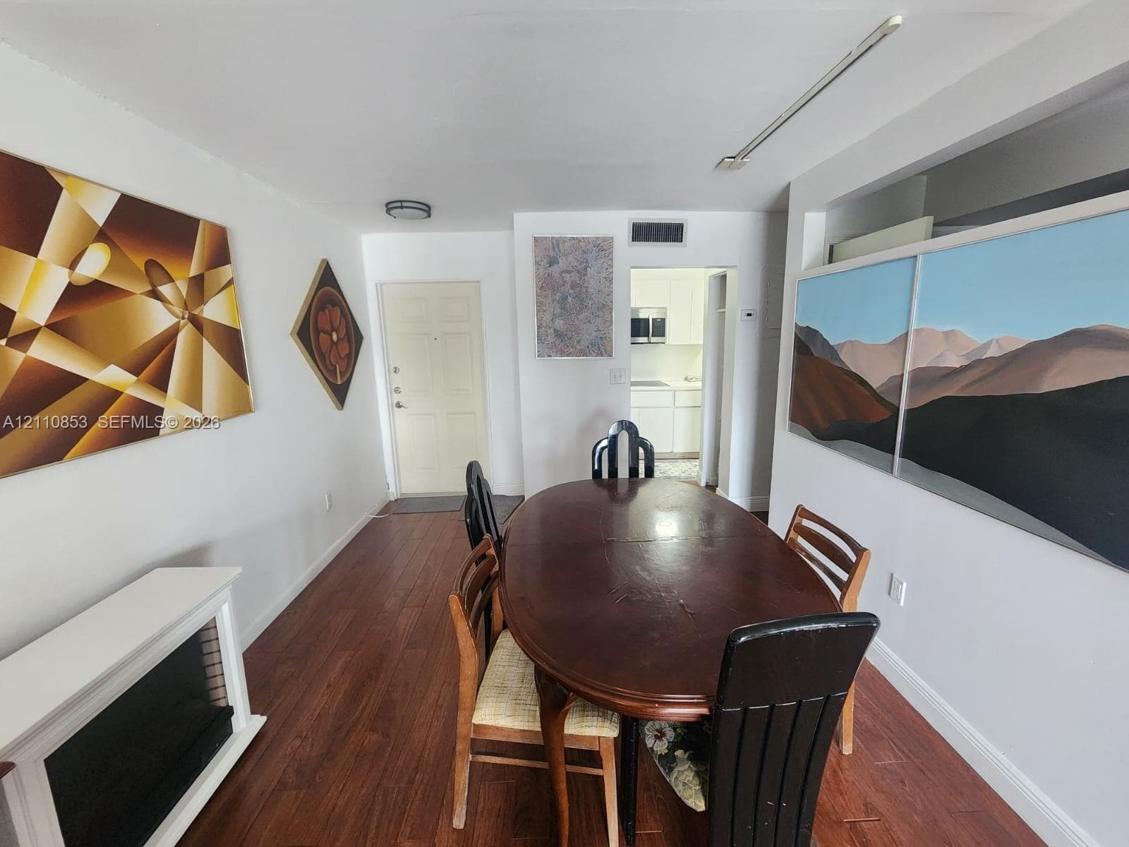 Wood-finish flooring, white fireplace surround, and interior doorway with visibility into the kitchen
