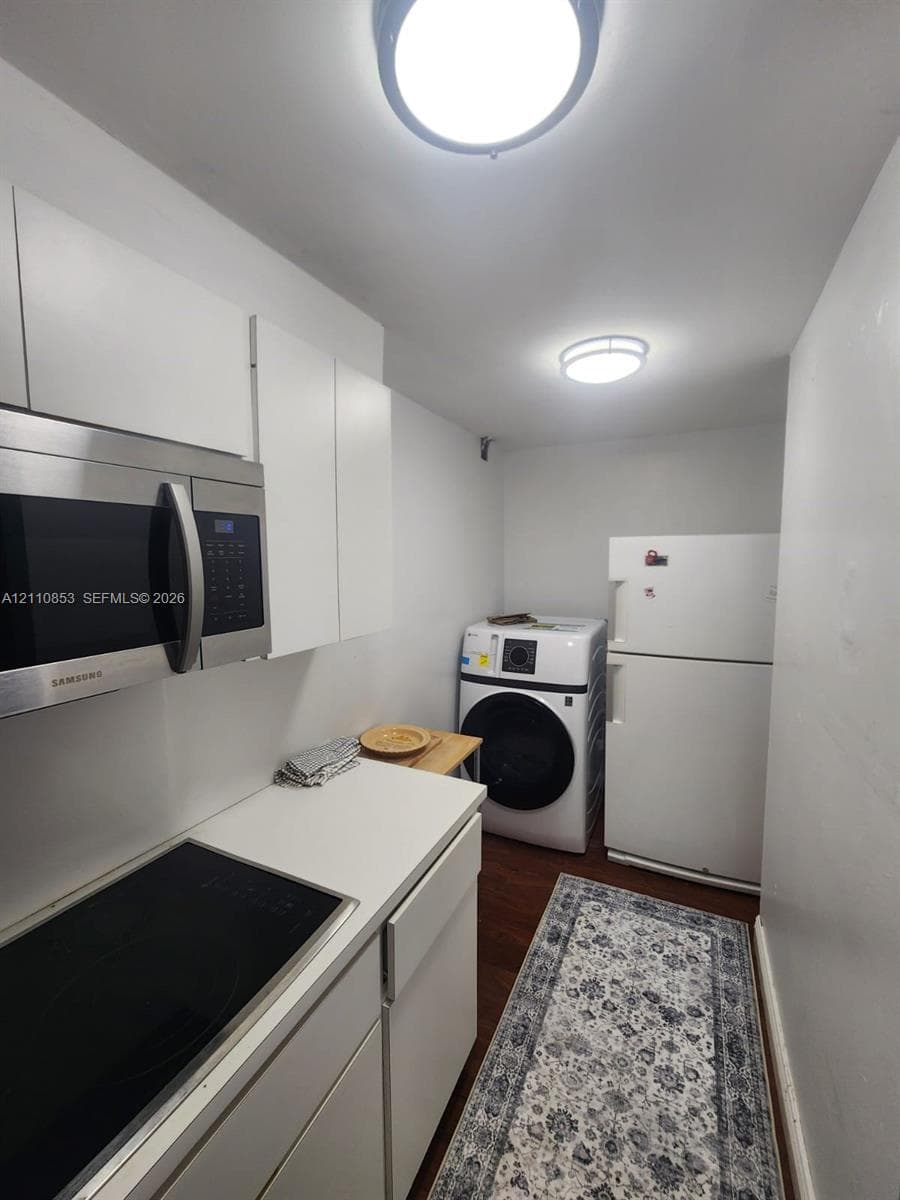 White cabinetry, solid-surface countertops, built-in stainless steel microwave, integrated electric cooktop, and wood-finish flooring