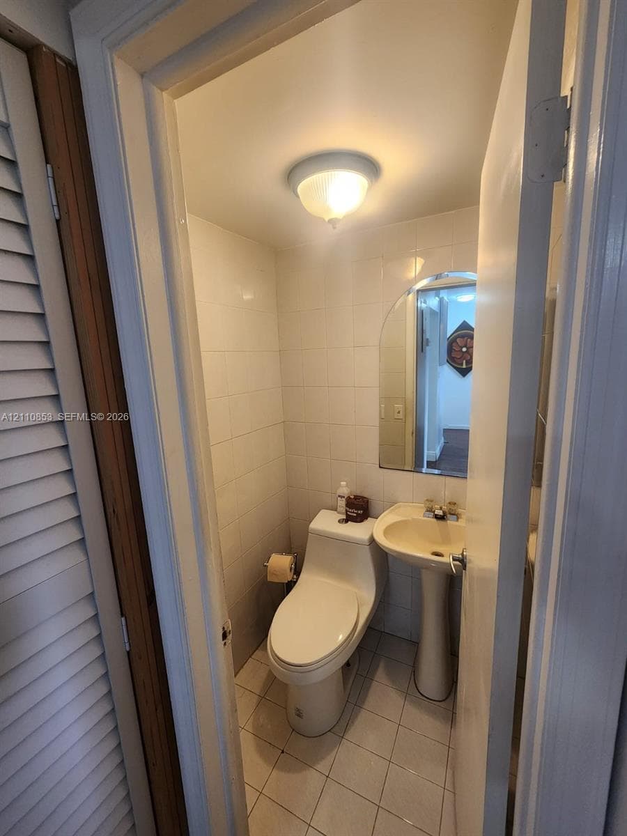 Half bathroom featuring a pedestal sink, arched wall mirror, ceramic tile flooring, and white wall tile