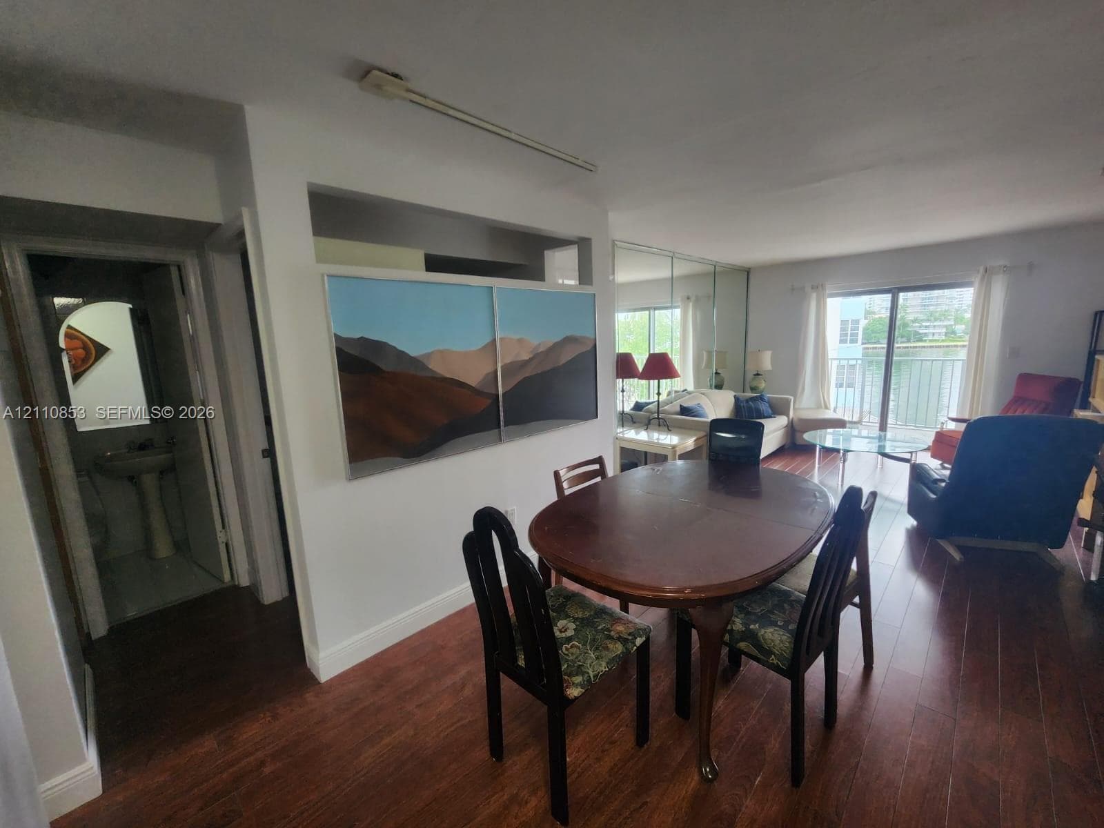 Open-concept interior featuring wood-finish flooring, a wall of mirrored panels, and a sliding glass door providing external access