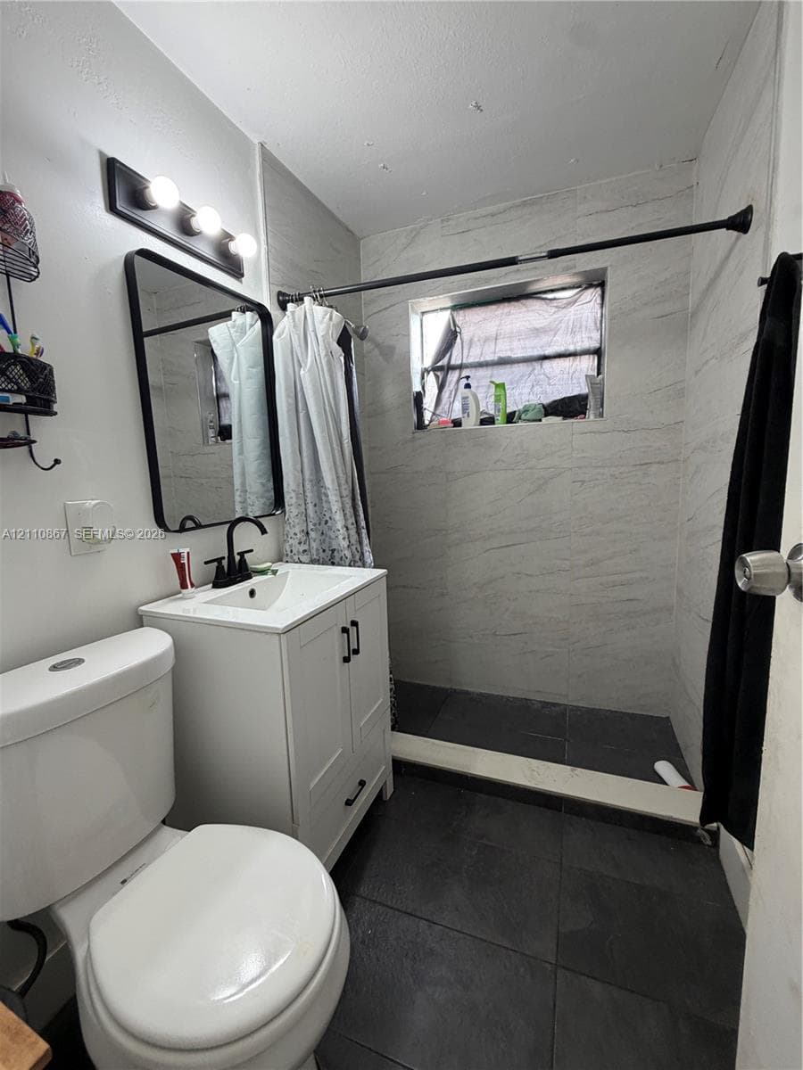 Bathroom featuring white cabinetry, a rectangular sink with matte black hardware, a black-framed vanity mirror, dark floor tile, and wall-tiled shower surround