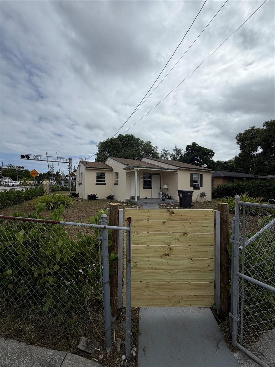Single-story exterior featuring a light-toned stucco facade, dual-pitched roofline, covered front entryway, and a wood-slat privacy gate