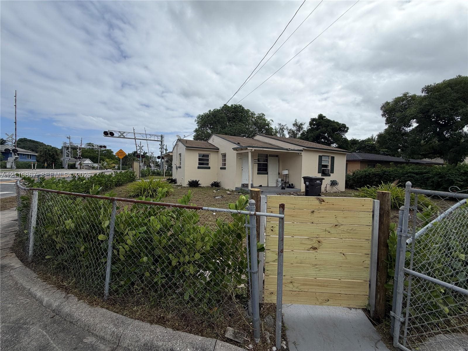 Exterior featuring a stucco facade, covered front entryway, and metal-framed chain-link fencing with a horizontal wood-slat gate