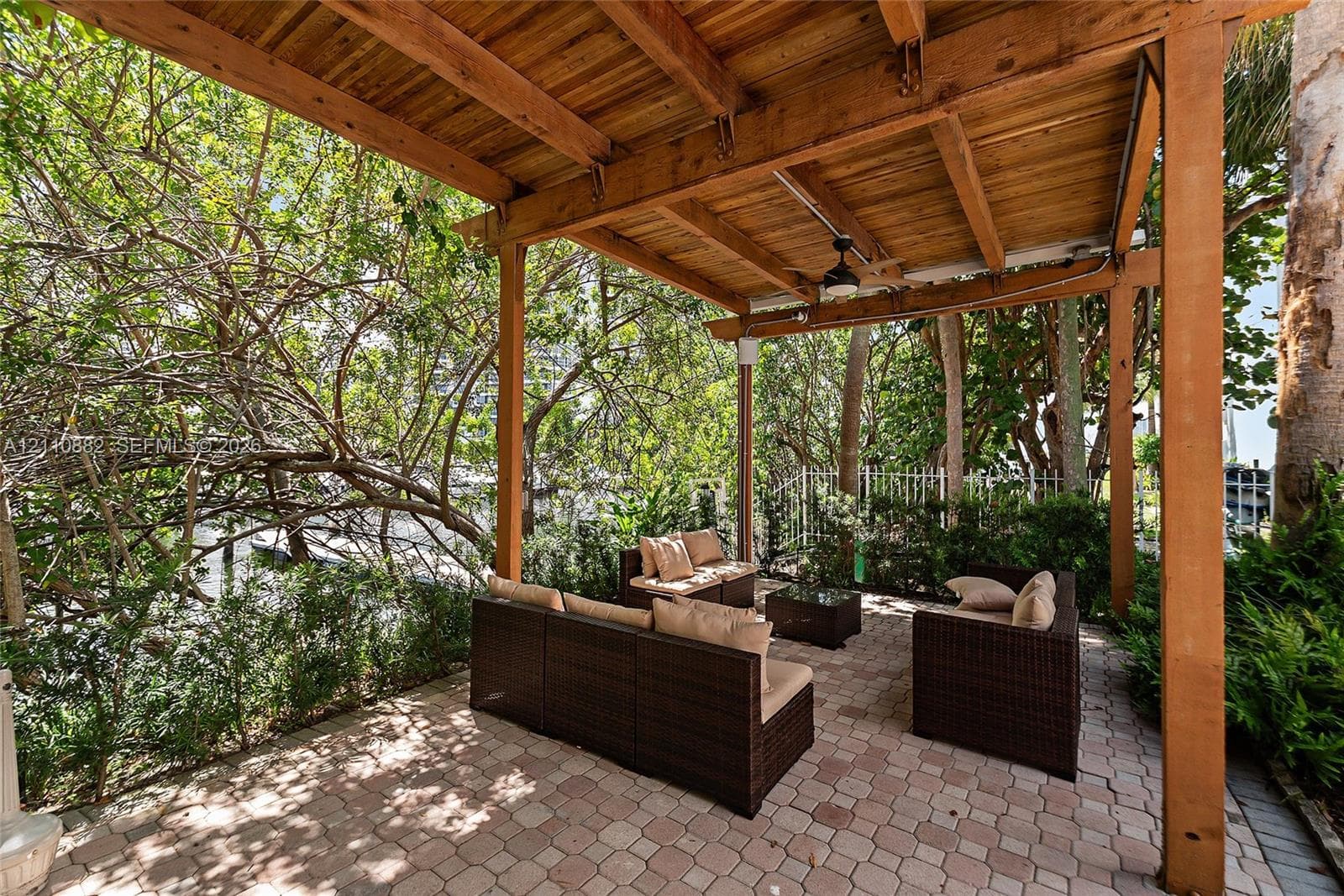 Covered patio featuring a wood-beam pergola, stone-paver flooring, and a ceiling-mounted fan