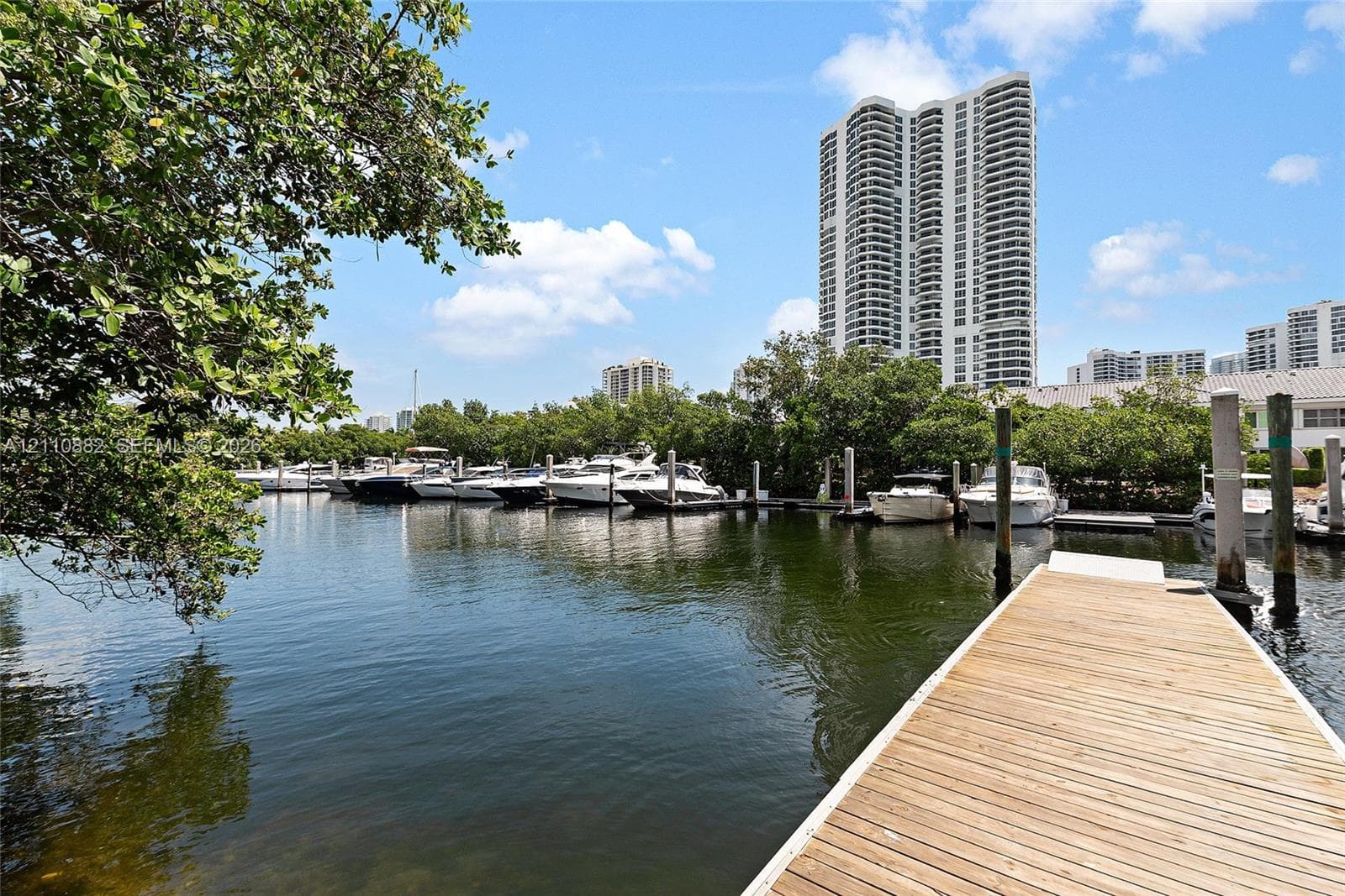 Waterfront dock featuring wood-plank decking and reinforced pilings, situated on a deep-water canal with mature perimeter trees
