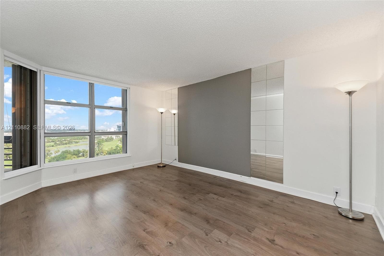 Large floor-to-ceiling bay windows, wood-finish flooring, and a decorative mirrored wall accent
