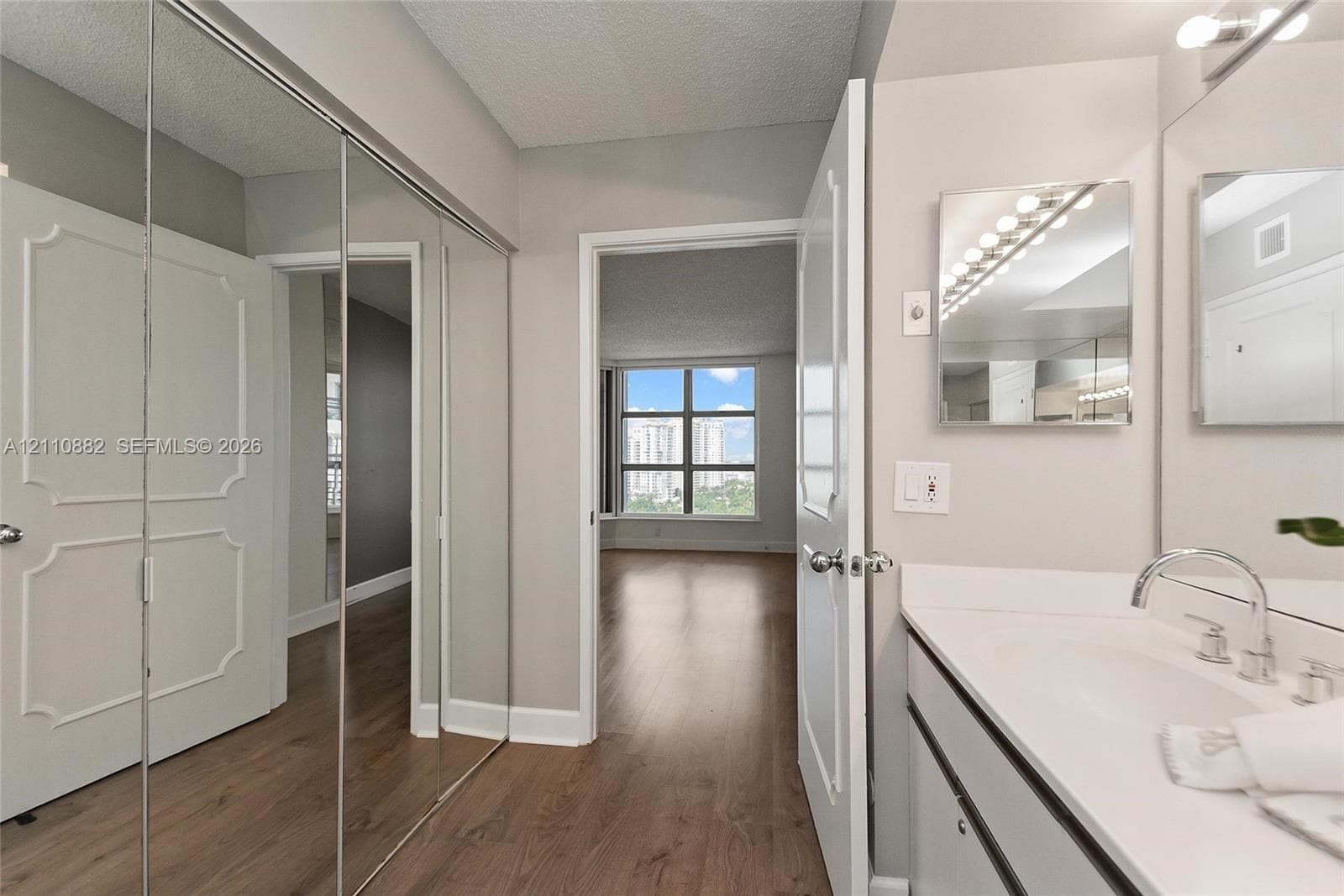 Bathroom featuring a vanity with a white countertop and undermount sink, wall-mounted mirror with integrated lighting, and full-length mirrored closet doors