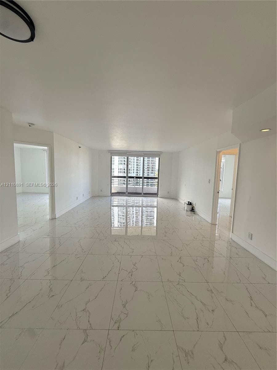 Large-format white tile flooring with grey veining, neutral wall finishes, recessed lighting, and floor-to-ceiling sliding glass doors featuring a metal frame
