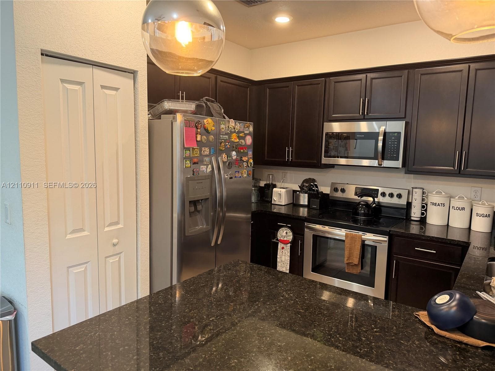 Dark finish cabinetry, dual-basin stainless steel sink, stone countertop, matte black faucet, and window with natural light