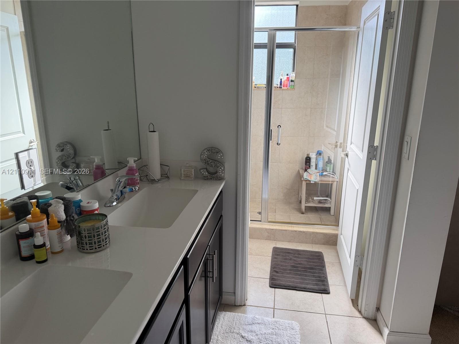 Vanity with dual integrated rectangular sinks, stone-finish countertop, dark cabinetry, and full-width wall mirror, featuring a walk-in closet with built-in shelving