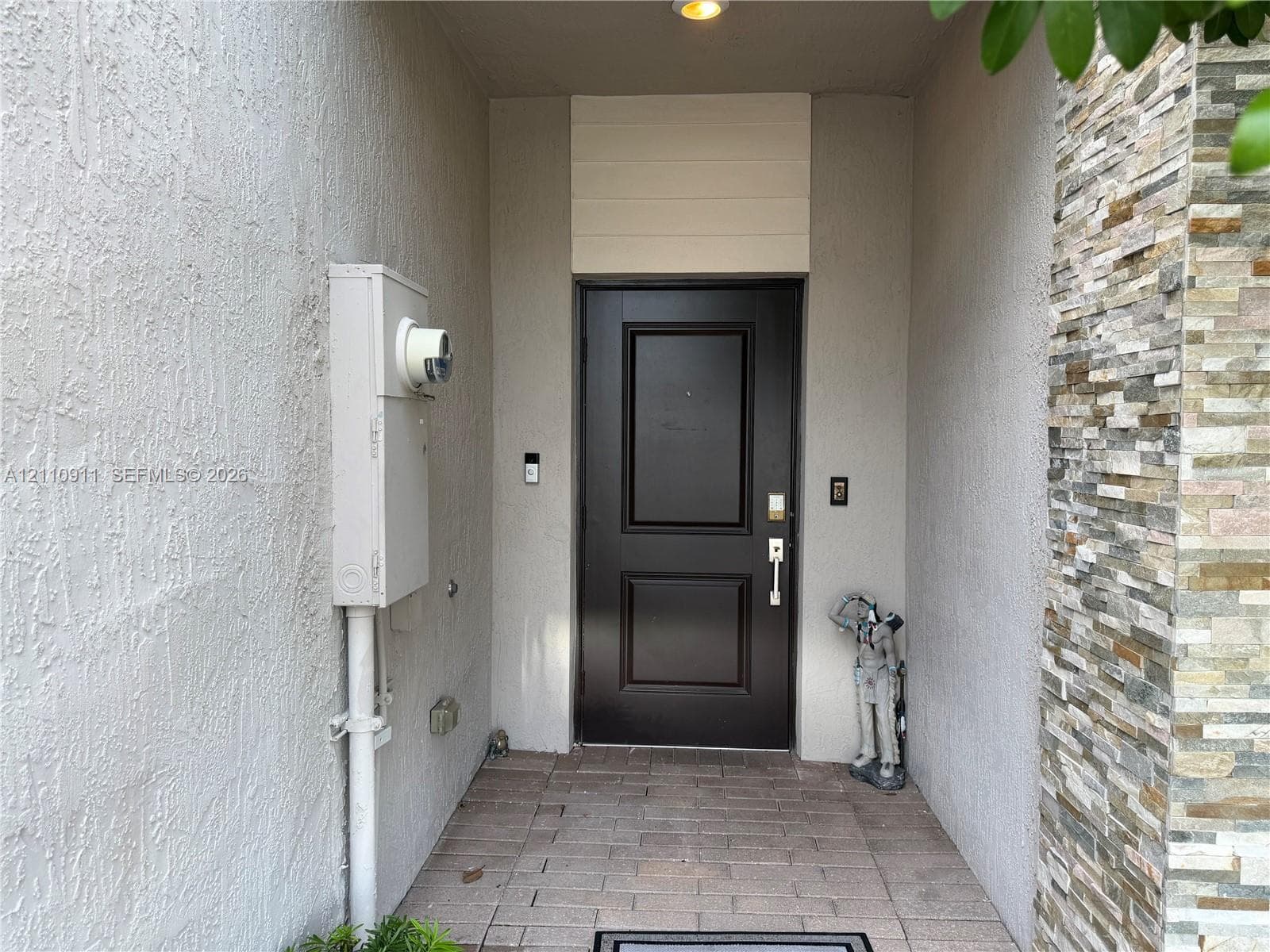 Contemporary two-story exterior featuring light-toned stucco siding, a paver driveway, an attached garage, and stone veneer accents