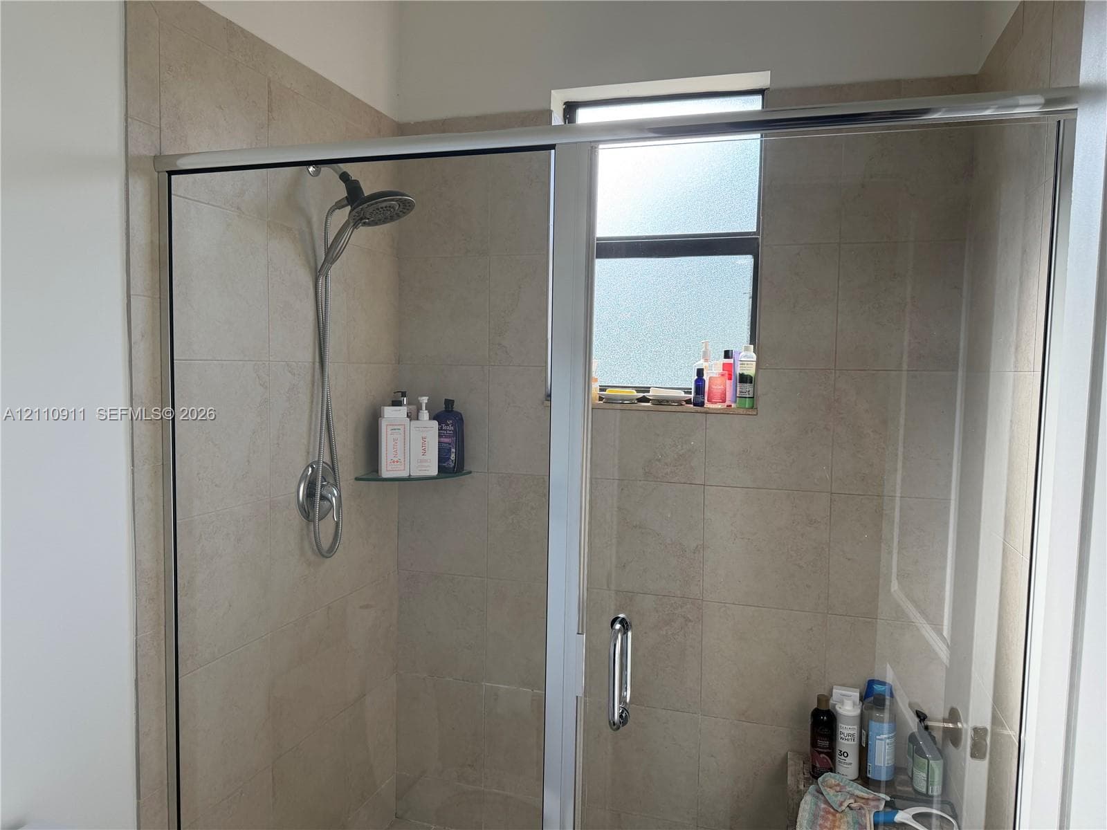 Dual-sink vanity featuring a light-toned solid surface countertop, rectangular undermount basins, dark-finished cabinetry with metallic hardware, and a full-width wall mirror