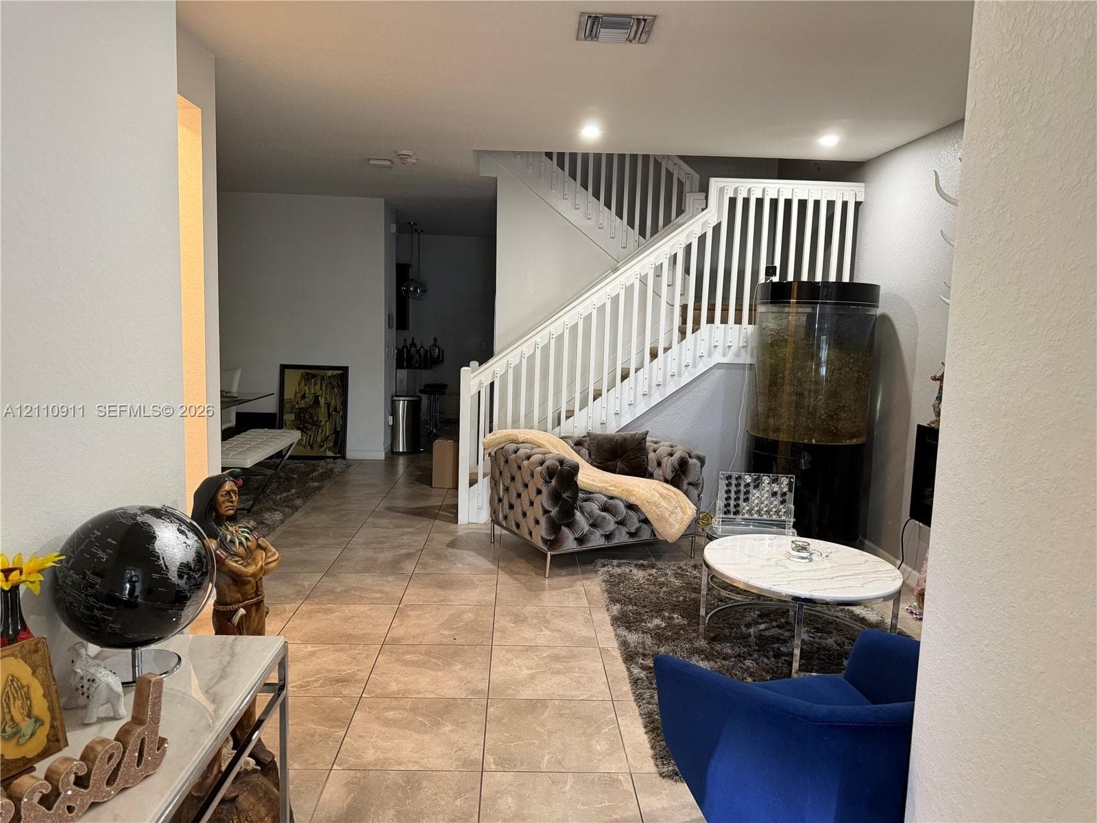 Neutral-toned walls featuring a recessed electric fireplace and light-colored tile flooring throughout, accented by recessed lighting and a window fitted with dual-layer cellular shades