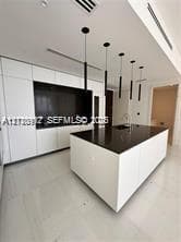 Modern kitchen featuring white flat-panel cabinetry, a central island with a dark countertop, recessed lighting, and a series of minimalist pendant lights