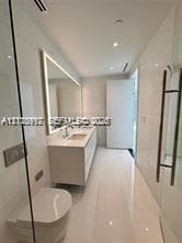 Modern bathroom featuring floor-to-ceiling tile, a floating dual-sink vanity with integrated lighting, a wall-mounted toilet, and a glass-enclosed shower