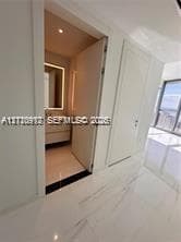 Large-format tile flooring, flush-mounted interior doors, and recessed ceiling lighting, with entry to a bathroom featuring a floating vanity and an integrated illuminated mirror
