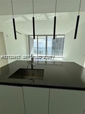 Modern kitchen island featuring a solid-surface countertop, integrated stainless steel undermount sink, gooseneck faucet, and four cylindrical pendant lights