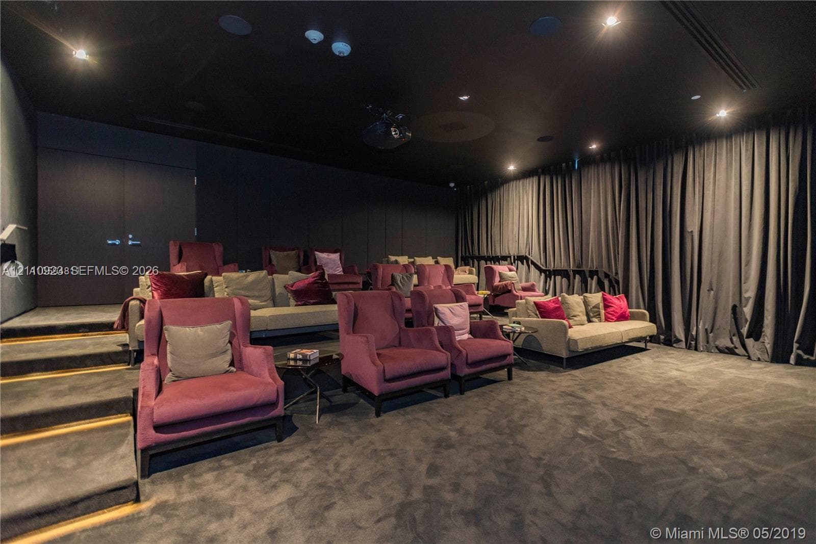 Dedicated screening room featuring multi-level stadium seating, floor-to-ceiling drapery, recessed ceiling lighting, and wall-mounted projection equipment