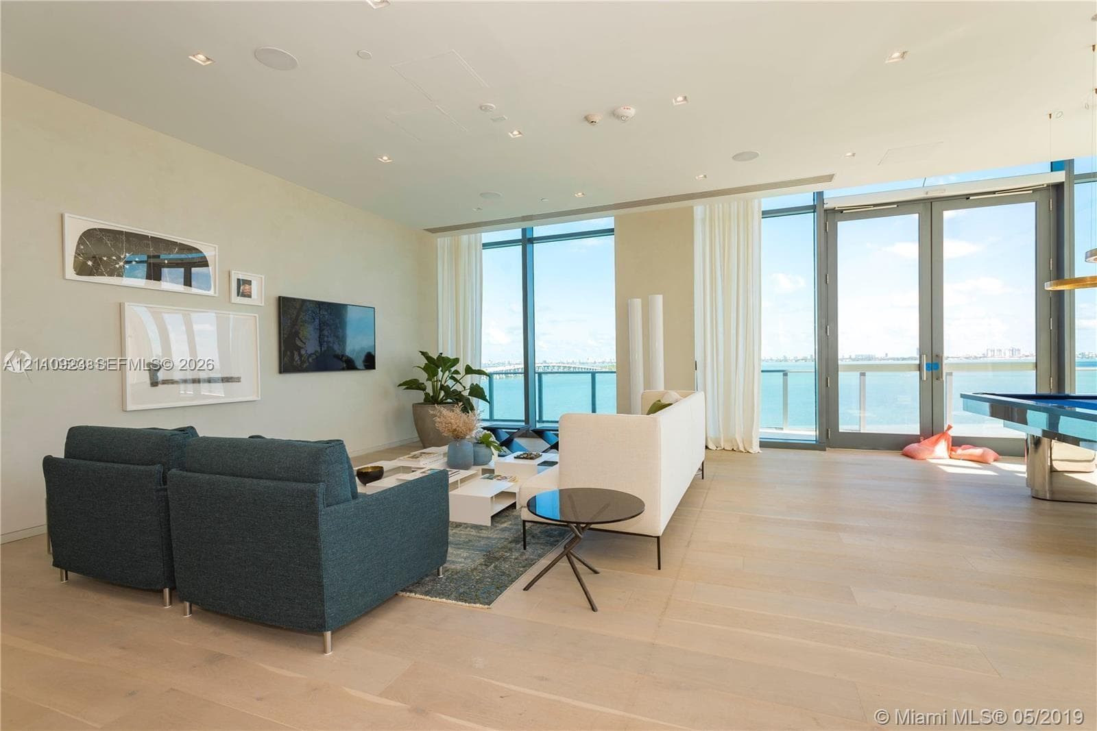 Expansive living area on 9th floor amenities level featuring floor-to-ceiling glass windows, wide-plank wood-finish flooring, recessed lighting, and full-height glass doors opening to the exterior