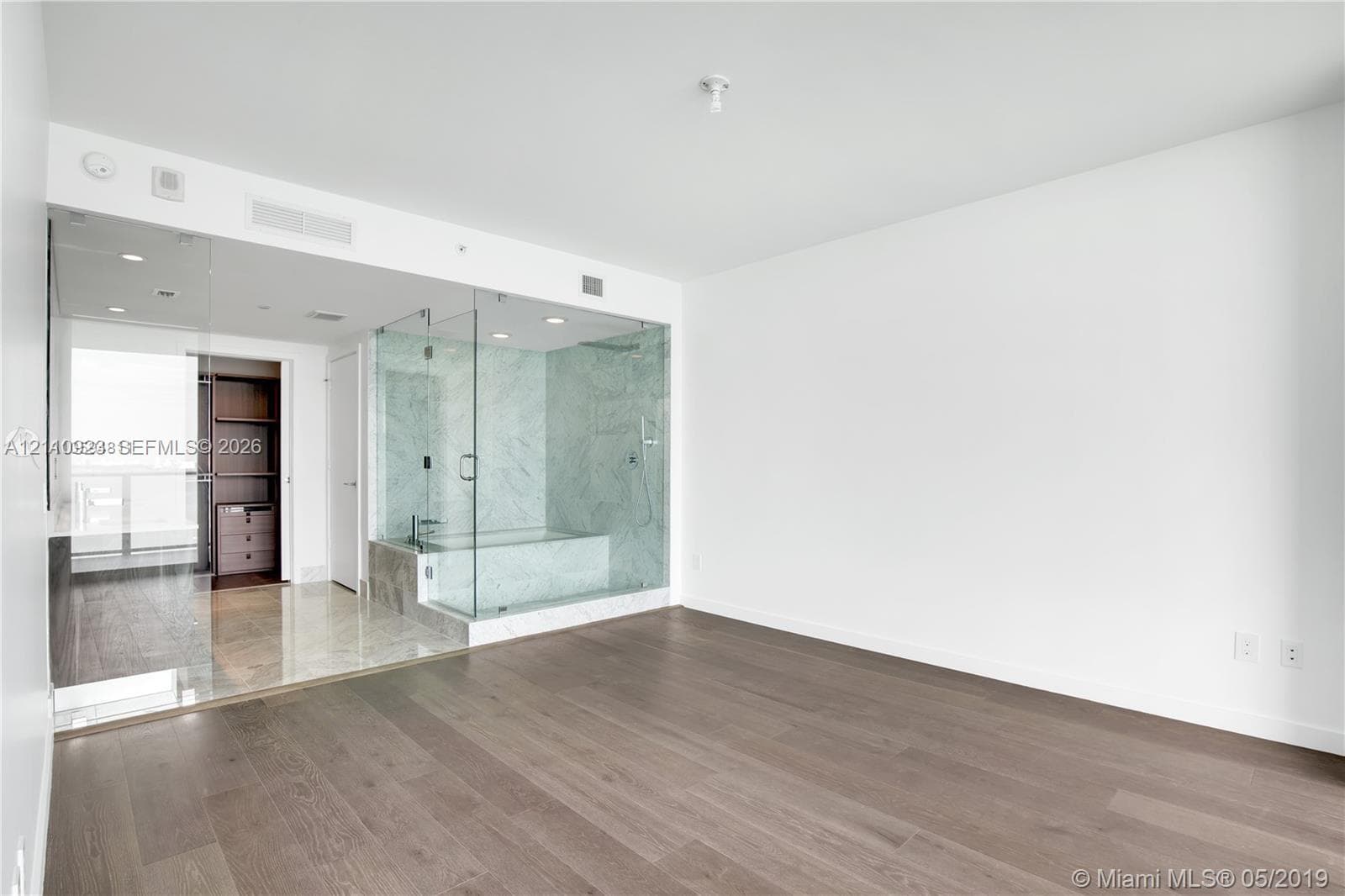 Open-concept interior featuring wood-finish flooring, glass-enclosed shower with stone-surround, built-in closet cabinetry, and recessed lighting