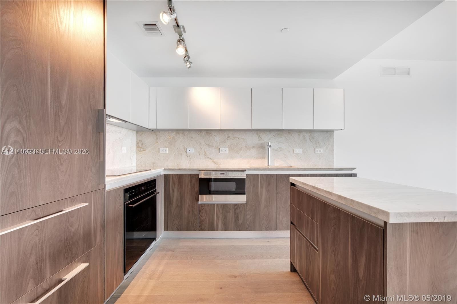 Kitchen featuring wood-finish cabinetry, stone-surface countertops, stone-pattern backsplash, stainless steel built-in oven, and track lighting