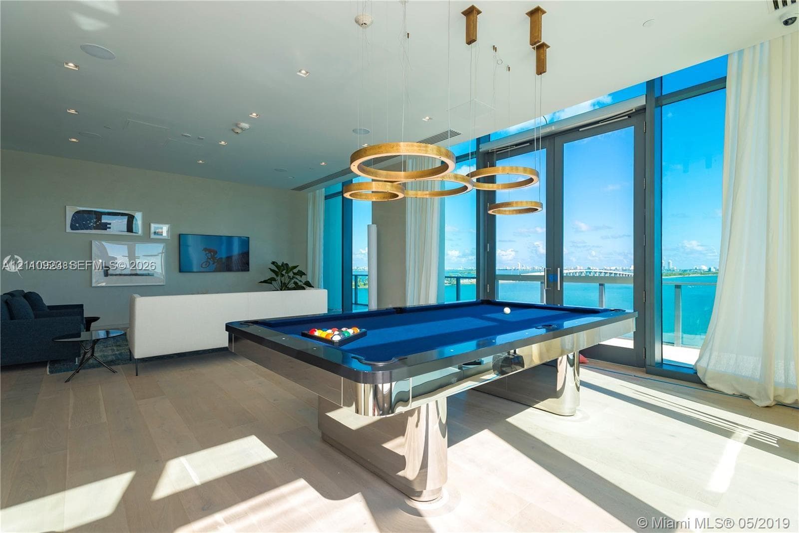 Floor-to-ceiling glass windows, recessed ceiling lighting, circular pendant light fixtures, and wood-finish flooring