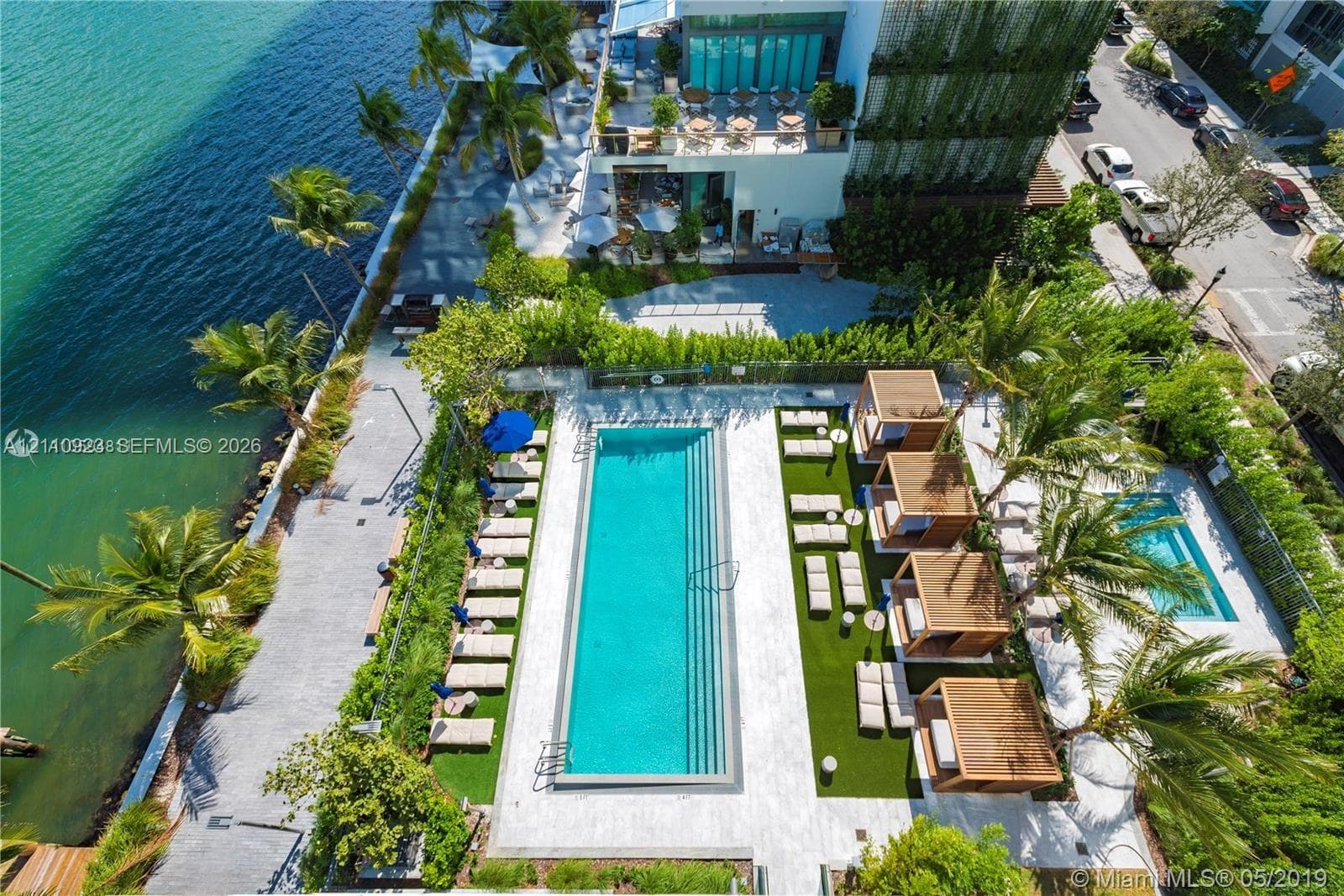 Waterfront swimming pool with tiered entry, paved sun deck, dedicated spa, and lush perimeter landscaping