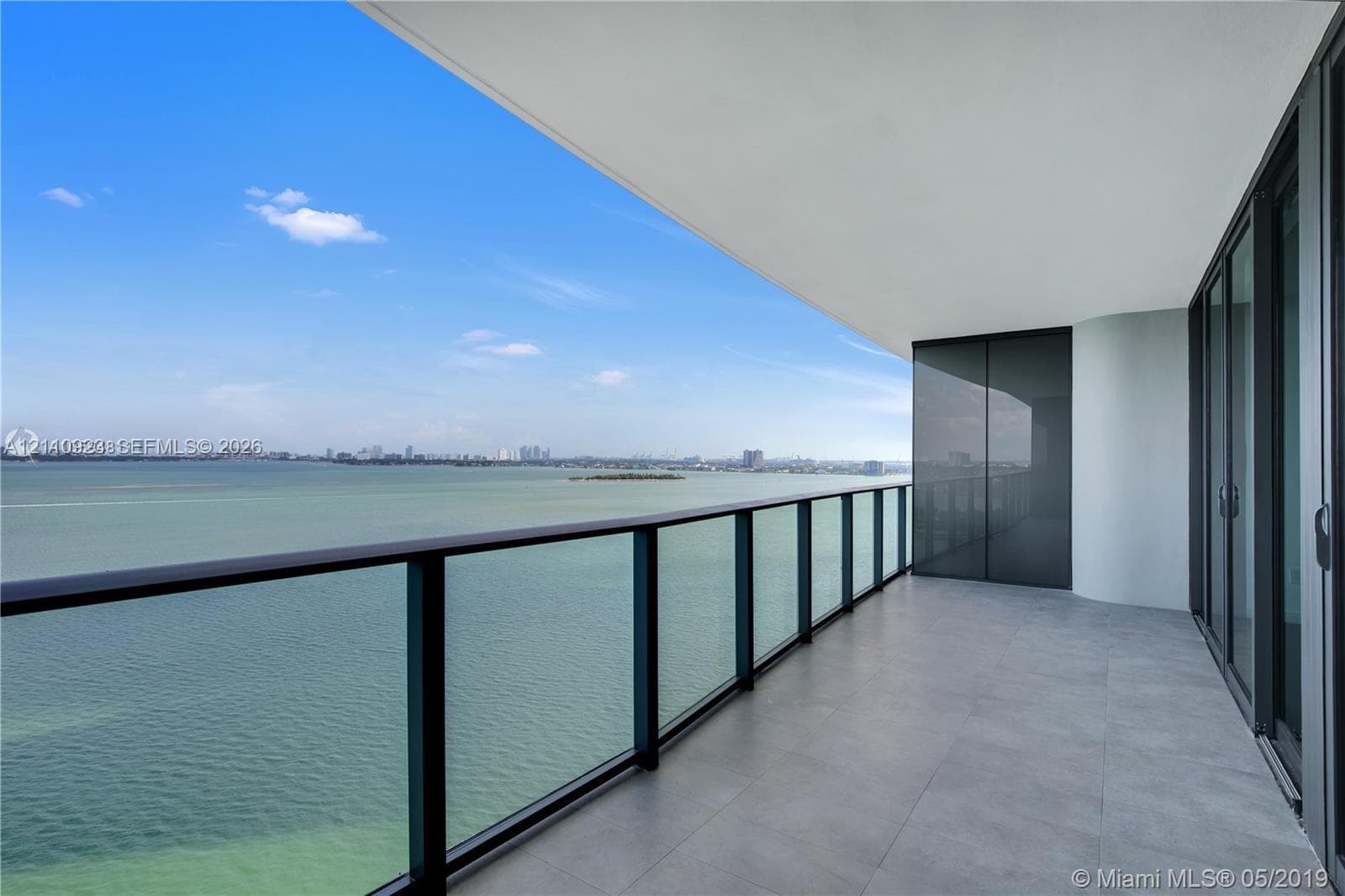 Expansive balcony featuring large-format porcelain tile flooring, black metal railing with glass panels, and sliding floor-to-ceiling glass doors