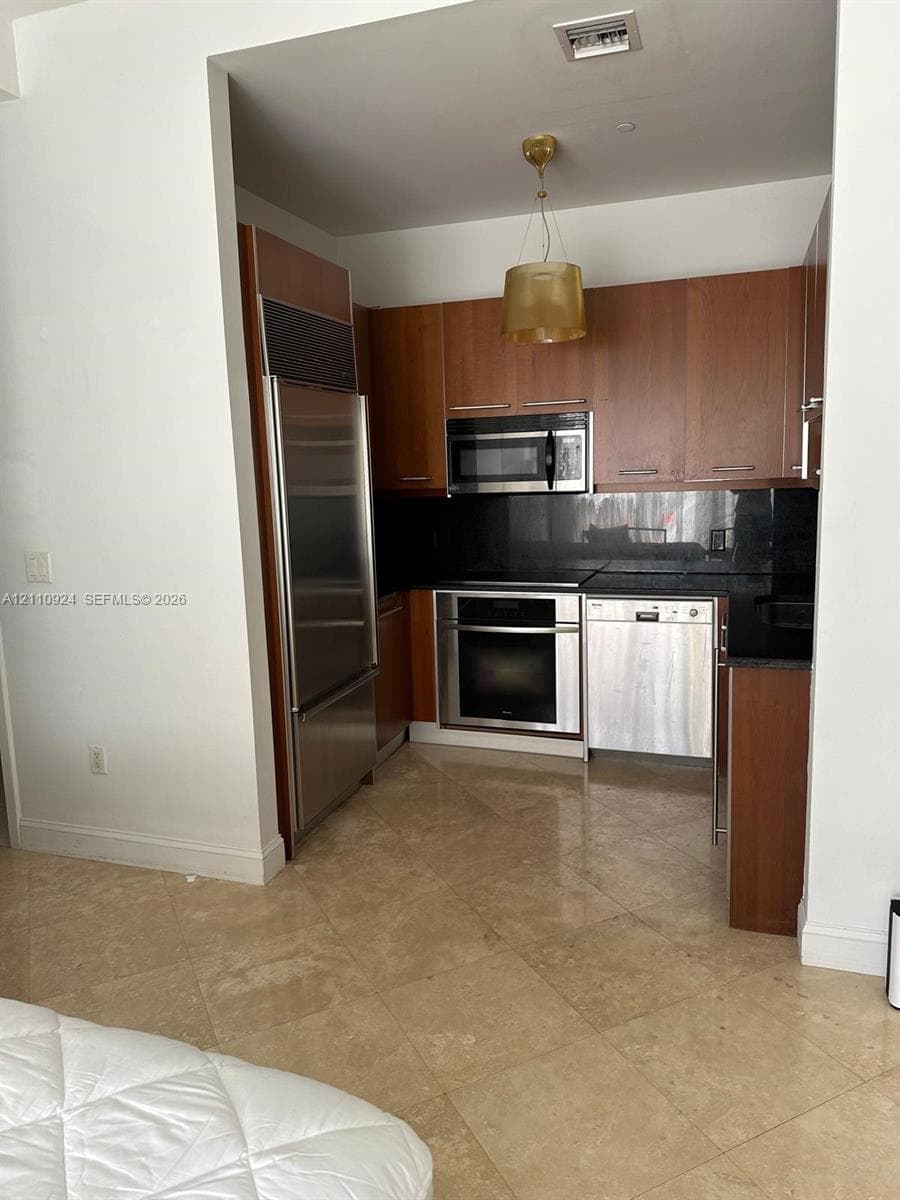 Kitchen featuring wood-veneer cabinetry, dark stone countertops, integrated stainless steel refrigerator, stainless steel built-in oven, and pendant lighting