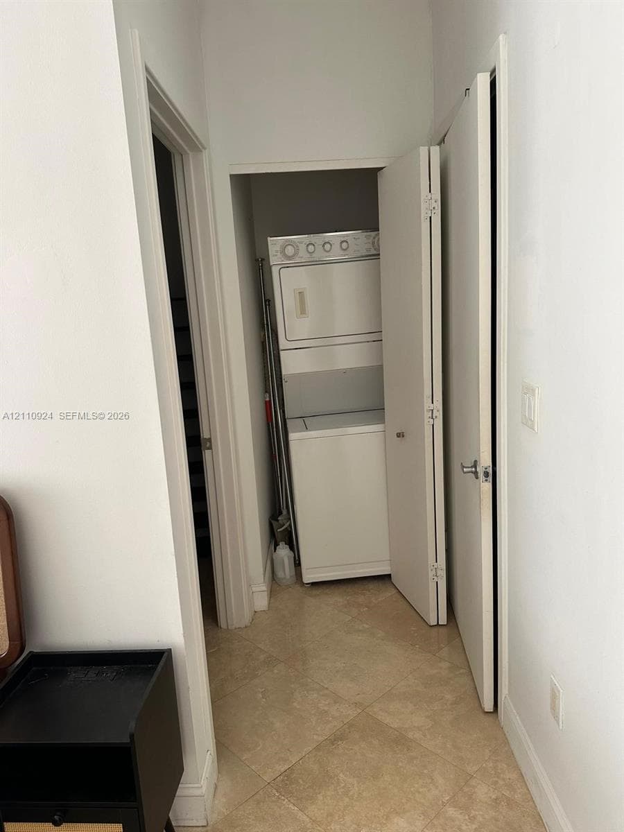 Stackable laundry unit housed in a dedicated closet featuring neutral-toned tile flooring and paneled interior doors