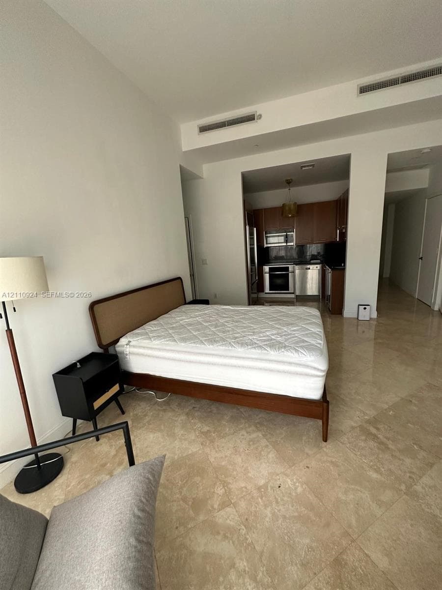 High-ceiling interior featuring polished stone flooring, recessed lighting, and a kitchen equipped with wood cabinetry and stainless steel appliances