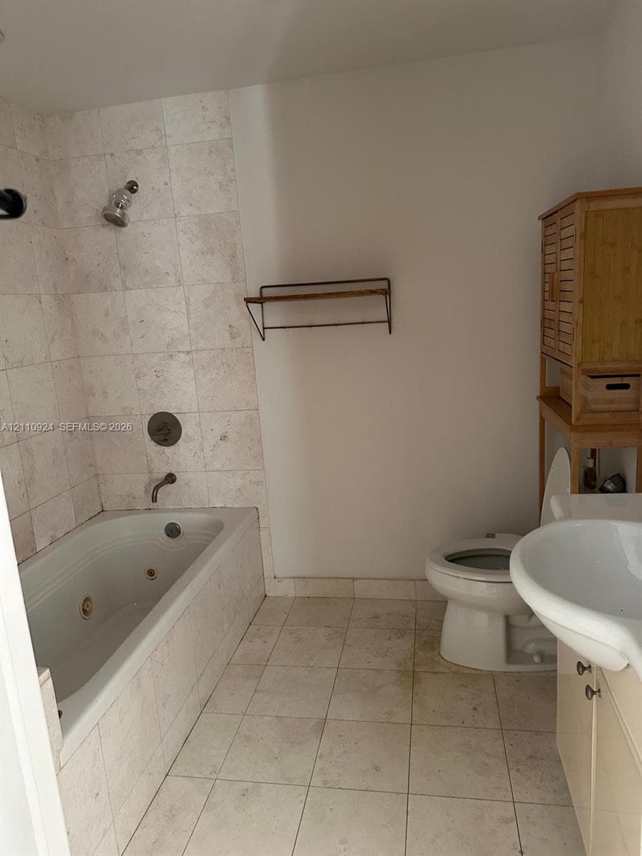 Bathroom featuring a jetted tub, wall-mounted shower fixture, ceramic tile surround, and ceramic floor tiling