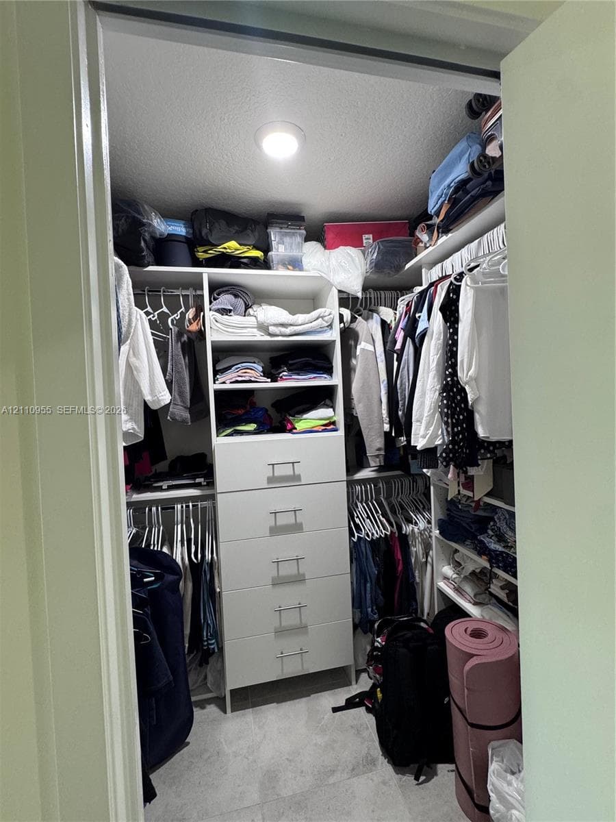 Walk-in closet featuring white built-in shelving, a five-drawer storage unit with metal pulls, dual-level hanging rods, and stone-finish flooring