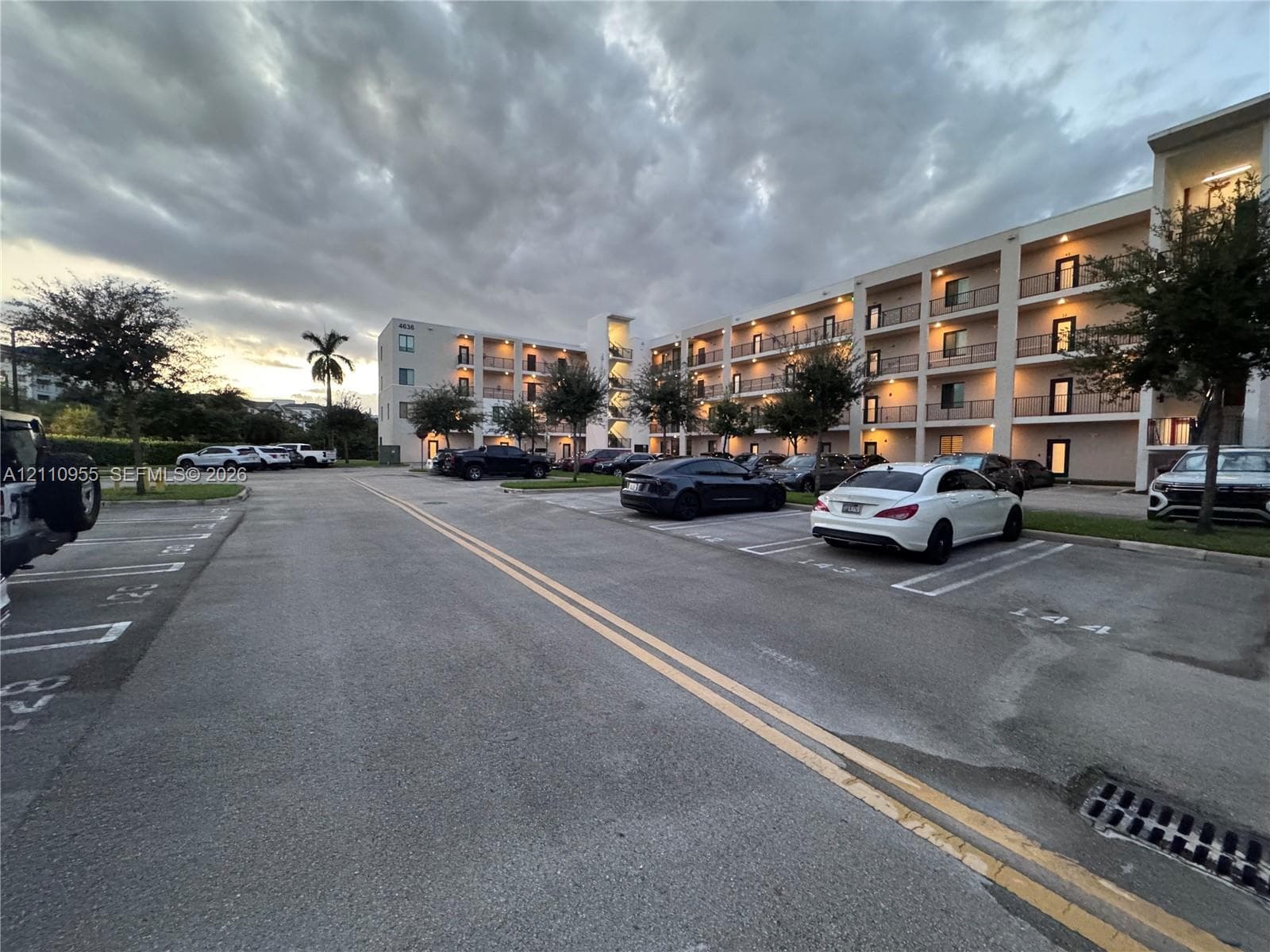 Multi-story residential building exterior featuring concrete facade, private recessed balconies, and paved surface parking