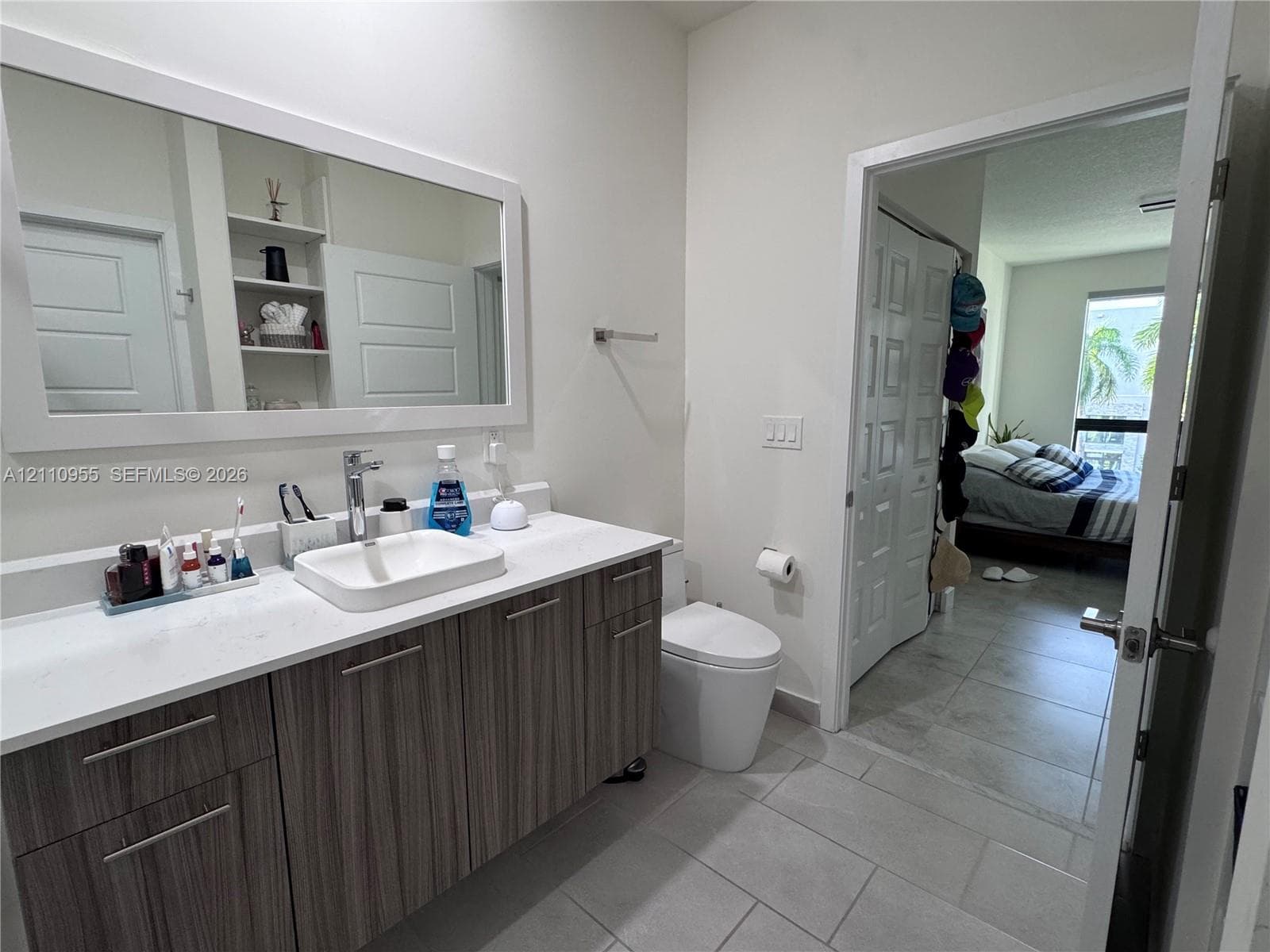Bathroom featuring a wood-finish vanity with a stone countertop, an integrated rectangular vessel sink, a large framed mirror, and tile flooring