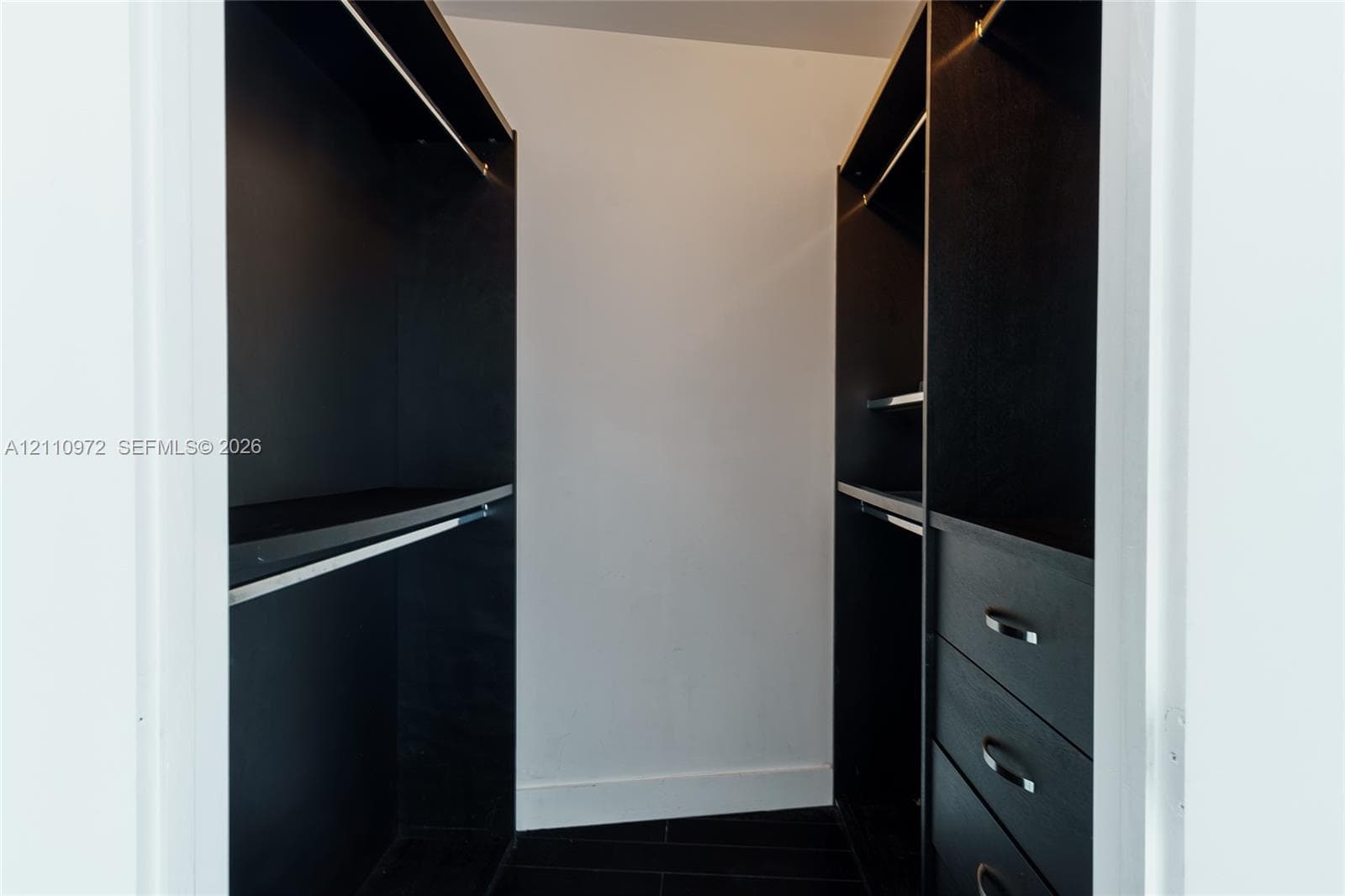 Built-in closet featuring matte black cabinetry, integrated shelving, hanging rods, and a three-drawer chest unit