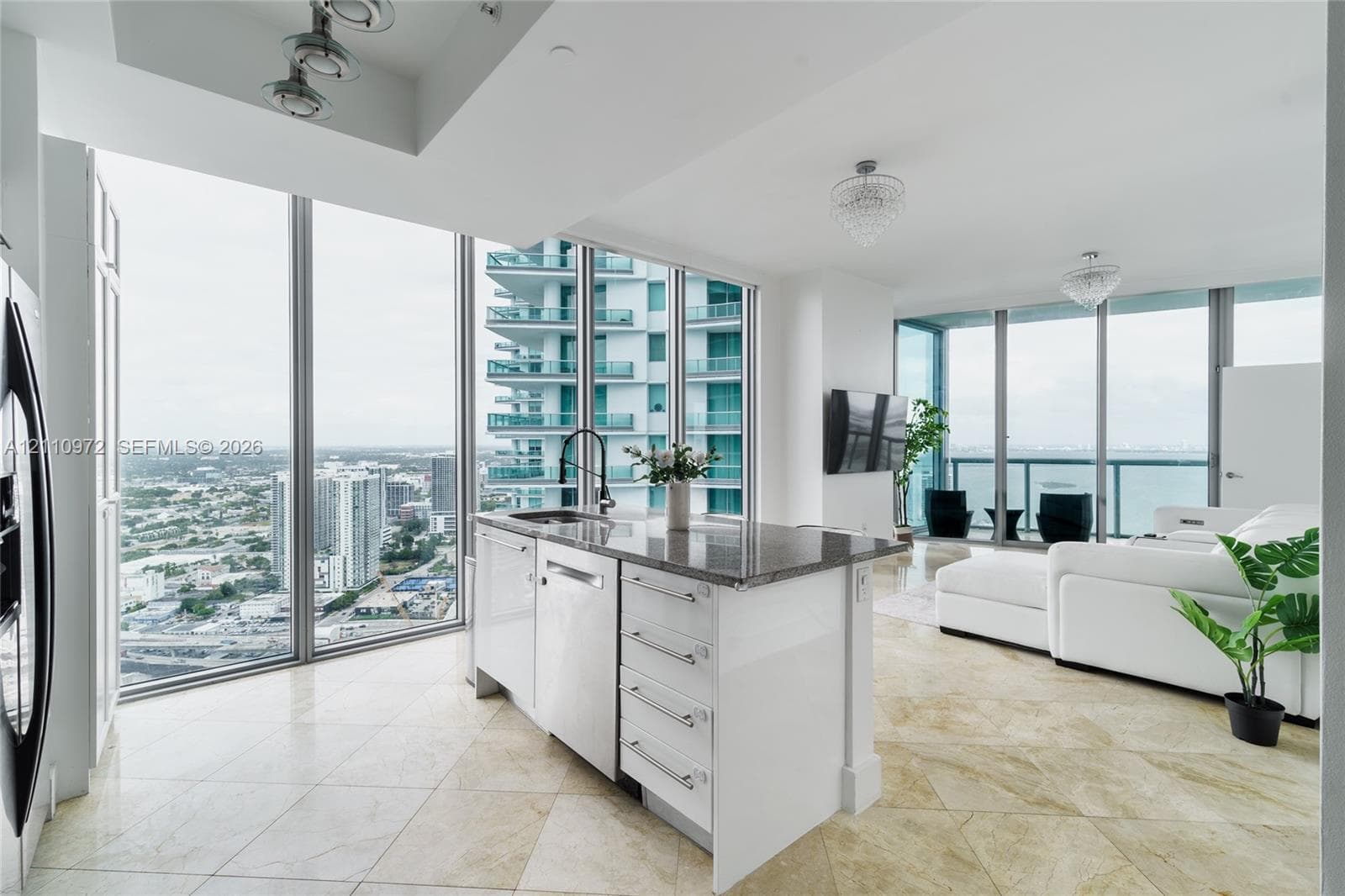 Open-concept kitchen featuring an island with stone-finish countertops, stainless steel appliances, floor-to-ceiling glass wall panels, and stone tile flooring
