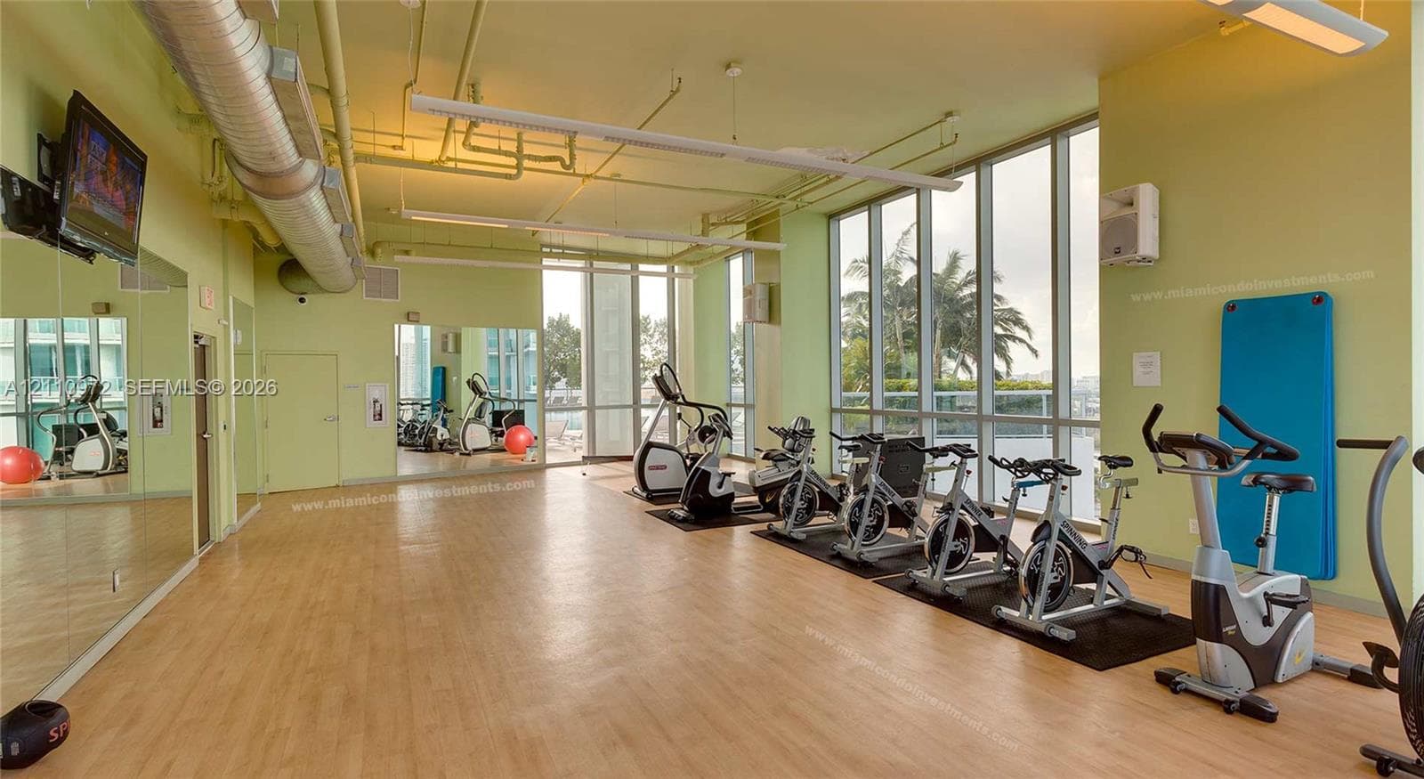 Fitness center featuring floor-to-ceiling windows, wood-finish flooring, full-length wall mirrors, and exposed industrial-style ceiling ductwork