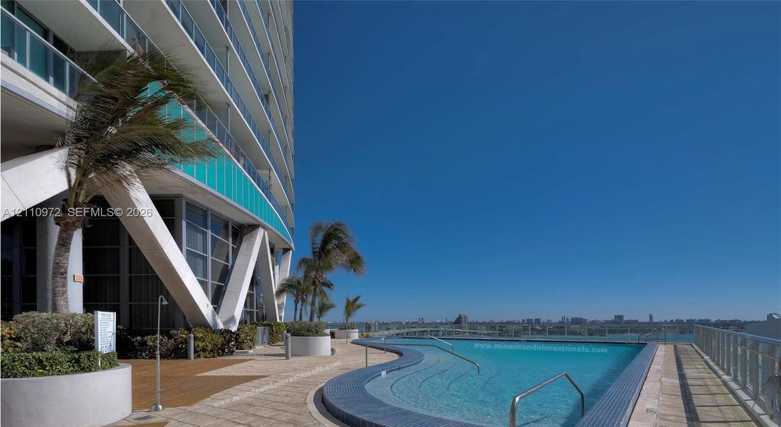 Outdoor pool featuring a curved tiled edge, tile decking, integrated tiered steps, and metal railings, set against an architectural facade with structural support beams and glass balcony partitions