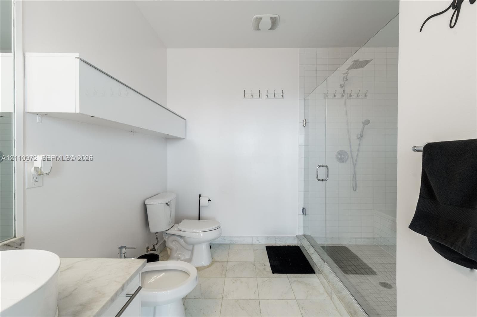 Bathroom featuring a stone-tile floor, a glass-enclosed walk-in shower with white tile surround, a wall-mounted white storage cabinet, and a vessel sink with a stone countertop