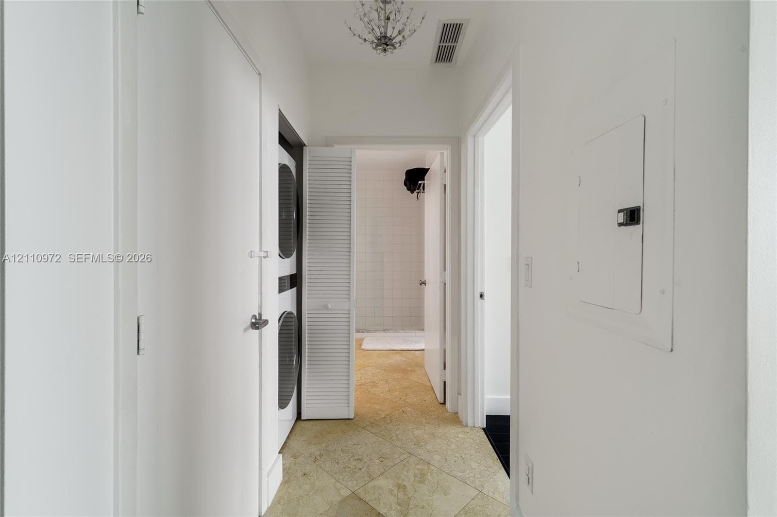 Hallway featuring stone-finish tile flooring, a decorative ceiling-mounted chandelier, and an integrated laundry closet with louvered doors